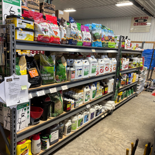 A store aisle with shelves displaying various gardening products, including grass seed, fertilizers, and pesticides. Bright packaging adds color to the scene.