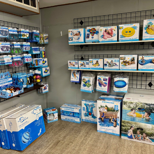 Wall displays of assorted pool accessories, inflatables, goggles, and games in colorful packaging. The setting is a store with a bright, inviting tone.