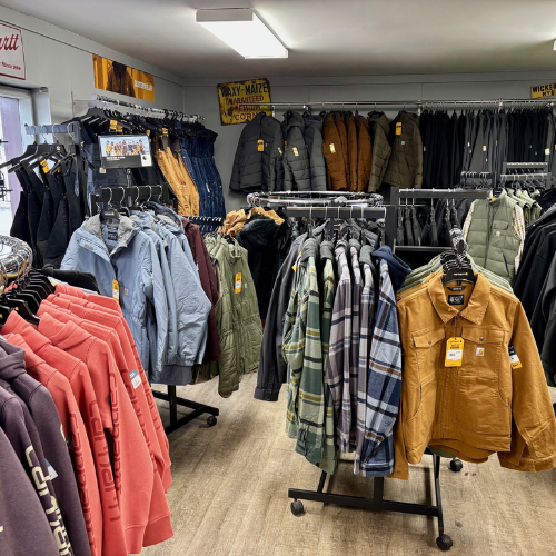 Clothing store interior with racks of jackets, hoodies, and flannel shirts. Earth tones dominate. Bright lighting and casual, organized ambiance.