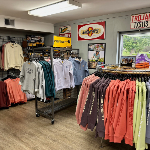 Clothing store interior displaying hoodies and sweatshirts on racks. Wall decor includes logo signs. Bright, welcoming atmosphere with natural light.