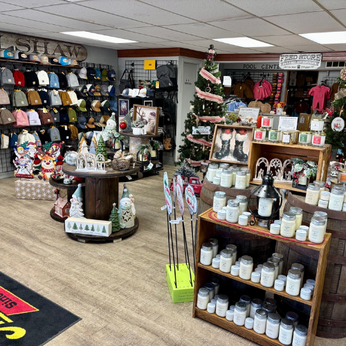 A cozy store interior features shelves of candles and holiday decorations. Hats and clothing line the walls, creating a festive and welcoming atmosphere.