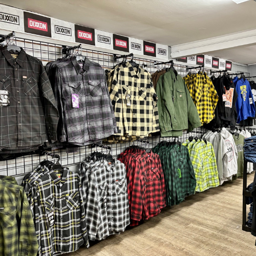 A store display features a colorful array of plaid shirts in various patterns and colors, neatly hung on a wall grid. The tone is vibrant and organized.